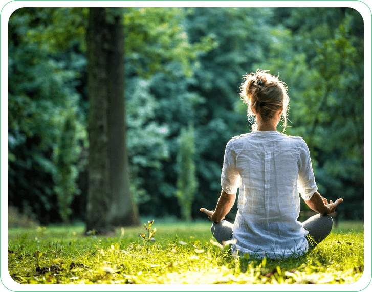 A woman sitting in the grass with her hands in yoga pose.